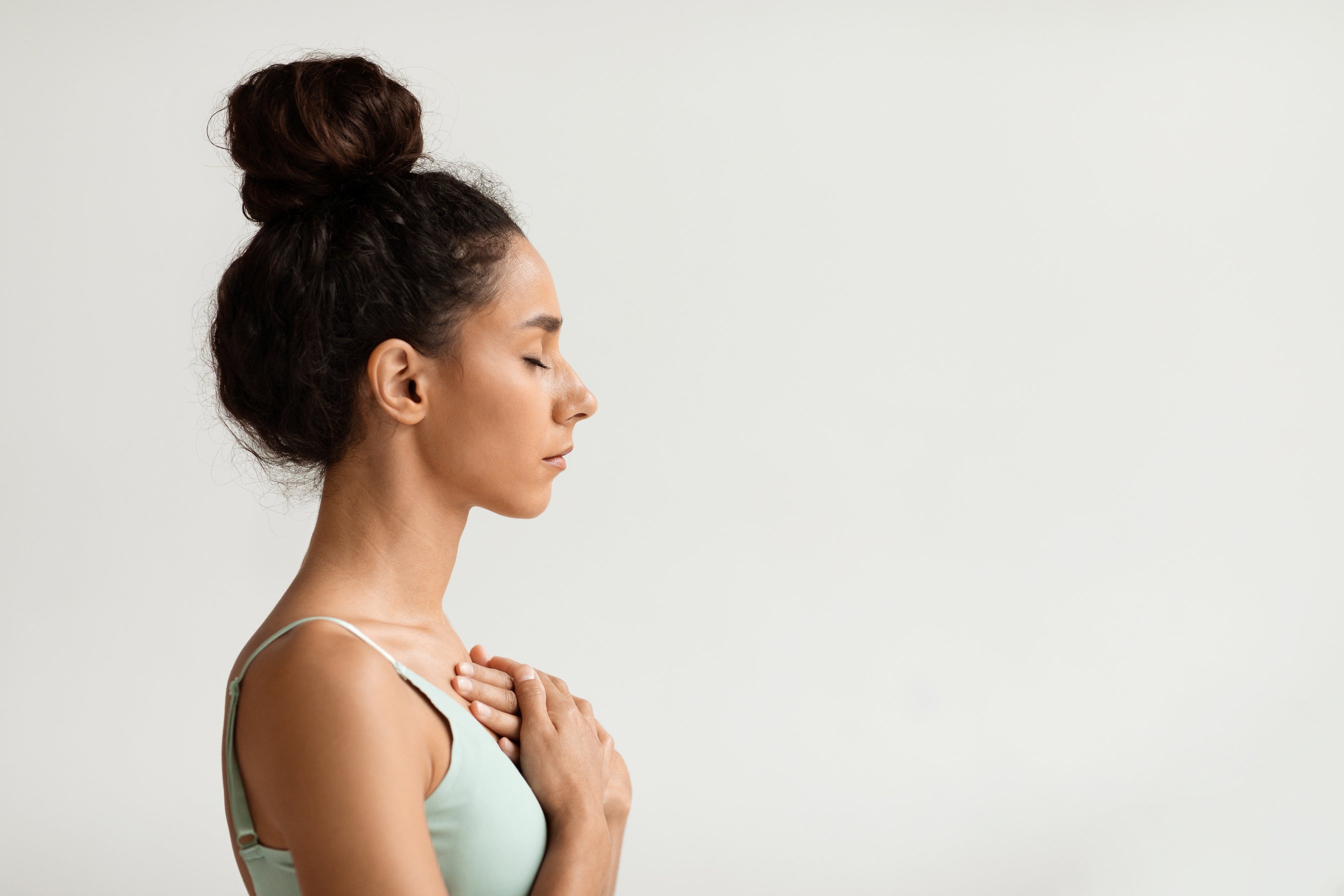 Profile of calm young woman with hands on chest and closed eyes